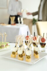 Many different tasty canapes on white table. People clinking glasses of wine indoors, closeup