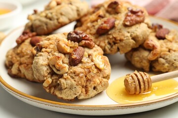 Tasty cookies with nuts and honey dipper on light table, closeup