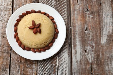 Delicious sweet semolina halva with almond on wooden table, top view. Space for text