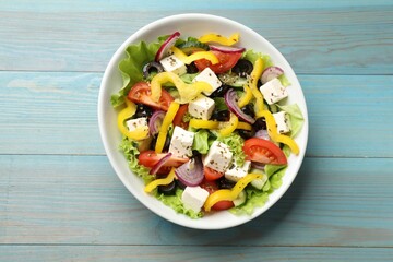 Delicious fresh Greek salad in bowl on light blue wooden table, top view