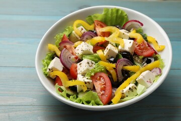 Delicious fresh Greek salad in bowl on light blue wooden table, closeup
