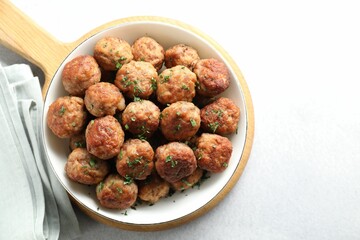 Tasty cooked meatballs with green onion in bowl on white table, top view. Space for text