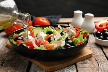 Adding olive oil to Greek salad at wooden table, closeup