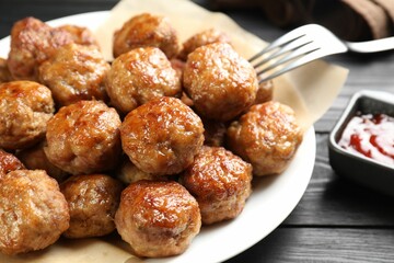 Many delicious meatballs served with ketchup on dark wooden table, closeup