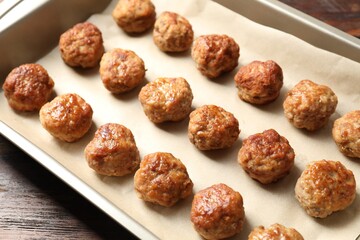 Many delicious meatballs in baking dish on wooden table, closeup