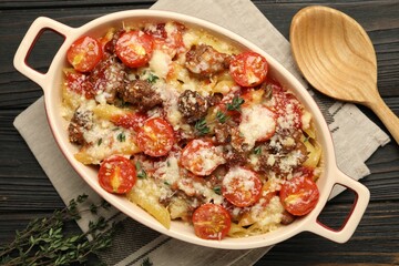 Delicious pasta casserole with cheese, tomatoes, minced meat and thyme in baking dish on wooden table, flat lay