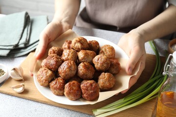 Woman holding plate with delicious meatballs at light textured table, closeup