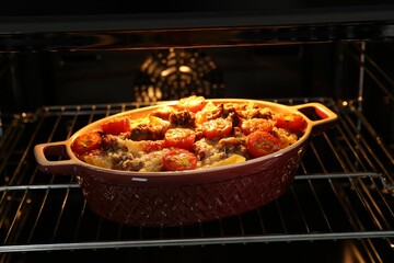 Delicious pasta casserole with cheese, tomatoes and minced meat in baking dish in oven, closeup