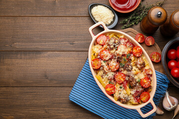 Delicious pasta casserole in baking dish with ingredients on wooden table, flat lay. Space for text