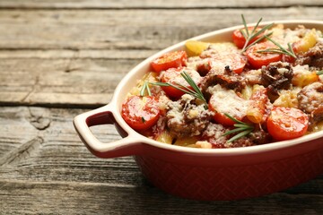 Delicious pasta casserole with cheese, tomatoes, minced meat and rosemary in baking dish on wooden table, closeup
