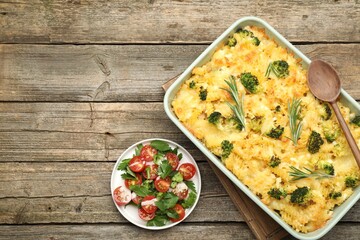 Tasty pasta casserole with cheese, rosemary, broccoli and salad on wooden table, top view. Space for text
