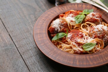 Delicious pasta with meatballs, cheese and basil on wooden table, closeup. Space for text