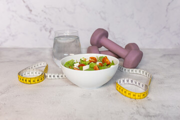 Healthy lifestyle concept with salad bowl, water, dumbbells and measuring tape. Diet concept.  