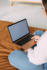 Fototapeta premium close-up photo of a girl working from home sitting on the bed holding a laptop on her lap