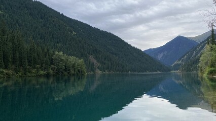 Mountains with pine trees are reflected in the calm surface of the water.