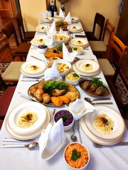A long dining table is set for a feast, laden with numerous dishes and neatly arranged white plates for a large gathering.