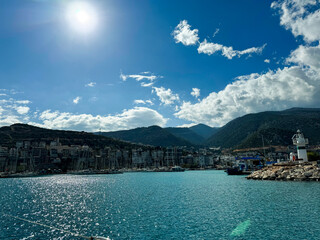 Coastal view of a vibrant harbor with boats and mountains under a clear blue sky