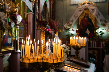Flame of lit candles. Many yellow wax candles on a candlestick. Holy liturgy in a church or temple. In the background an icon of Jesus