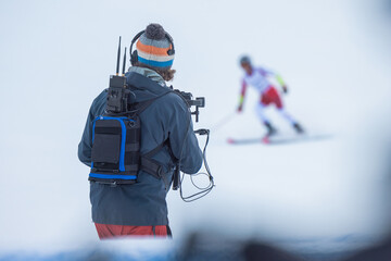 Back view of a cameraman using a gimbal or stabilizer for camera on a sports race. Visibile skier in blurred background just finishing the race.