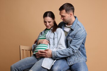 Man trying to feel baby kicks in his pregnant wife's belly on beige background