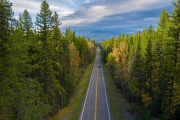 Autumnal highway through a dense forest. A car travels along a two-lane road, surrounded by vibrant fall foliage. , Big Fork, Montana, USA.