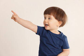 Cute little boy pointing at something on light grey background