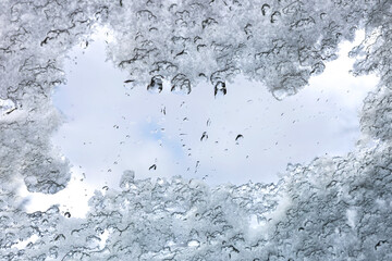 Melting snow and ice revealing a patch of clear sky. Close-up of melting snow and ice on a transparent surface with water droplets, framing a patch of clear blue sky. Copy space.