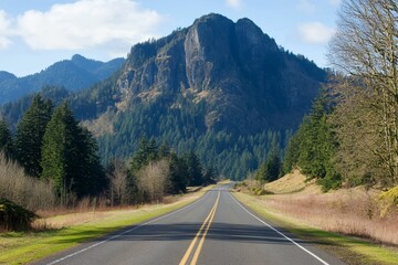 Fototapeta premium Asphalt road curves toward a large, forested mountain.