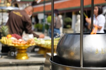 Phra Nakhon, Bangkok, Thailand - Nov 01, 2023: Employee at the Grand Palace lighting incense and preparing religious offerings of flowers, fruit, eggs and dried fish at a shrine inside Wat Phra Kaew 
