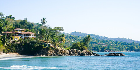 Obraz premium Lush coastal landscape with tropical trees, blue ocean, and vibrant hillside houses