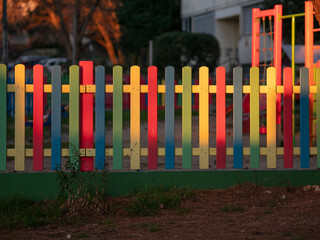 The colorful painted wooden boards on the fence around a playground are illuminated by the rays of the setting sun. Pula, Croatia - January 3, 2025