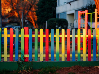 The colorful painted wooden boards on the fence around a playground are illuminated by the rays of the setting sun. Pula, Croatia - January 3, 2025