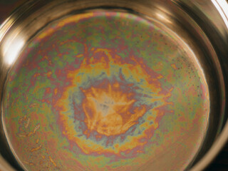 Iridescent color spots on the bottom of a stainless steel pan. Light interference in thin films. Concept of optical effects on familiar objects. Visual physics on kitchen household things