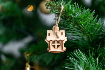 Close-up of wooden house-shaped Christmas ornament hanging on green pine tree branch, decorated.