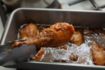 A view of tongs holding a slow cooker chicken drumstick.