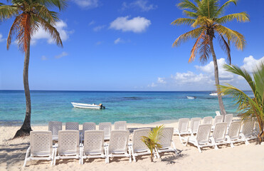 Beautiful beach with white chairs and white sand on the foreground and blue sky on the background on Saona Island, Dominican Republic