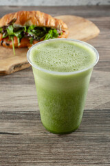 A view of a green vegetable smoothie, in front of a croissant sandwich.
