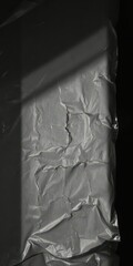 Crinkled plastic film, uneven surface, shadows, dark backdrop, close-up, photography, low-key