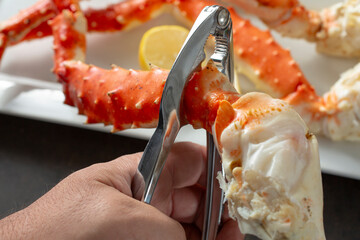 A view of a hand using a crab cracker tool on some king crab legs.