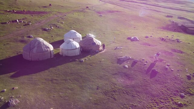 An aerial circling view of yurts and a horse in the remote mountains of Kyrgyzstan in early morning.