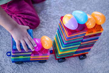 Toddler building a train with magnetic tiles and easter eggs