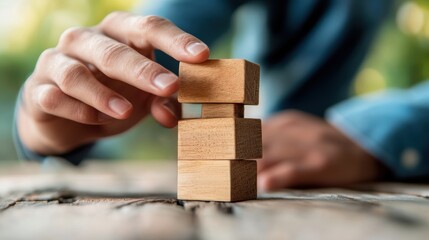 A person carefully stacking wooden blocks, focusing on balance and precision, set against a blurred natural background.
