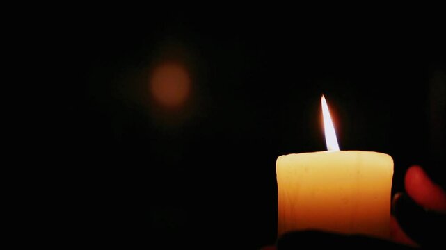 Woman extinguishes a candle against a dark background with blurred lights behind and empty space. Person blow out candle flame on black background. Finish of magical ritual with the fire of candle.