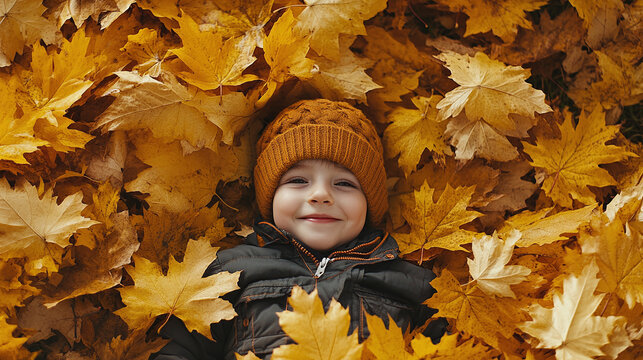 Top view of happy smiling toddler boy lying in pile of orange yellow autumn fall leaves in forest park nature. male preschool child or kid, september october foliage, outdoor, childhood, leisure.