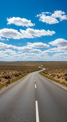 Naklejka premium A winding asphalt road stretches across a vast open countryside landscape with a bright blue sky and fluffy white clouds above The wide angle perspective creates a scene