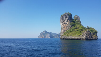 Seascape featuring towering limestone cliffs covered with lush green vegetation, rising from the crystal-clear blue waters