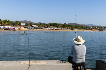 Panorama of the beach in Jalisco, Mexico in which a fisherman can be seen catching fish from the beach boardwalk
