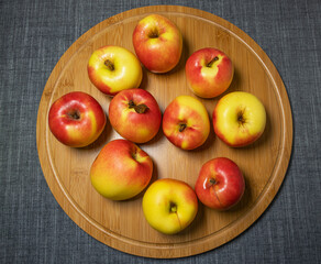 Beautiful fresh juicy red and yellow garden apples lie on a round bamboo cutting board, top view.