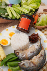 Jar of red chili paste with with orange label arrange on plate of cooked fish, white rice, boiled egg and vegetables
