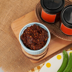 Close-up shot of a bowl of thai chili paste on wooden cutting board and jars with orange labels